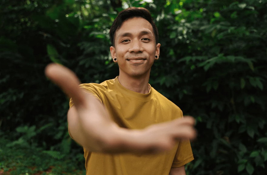 Bayu extending his hand out to the camera smiling in a yellow top.