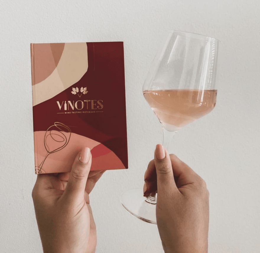 Hands holding a glass of rose wine in one hand and a notebook in the other